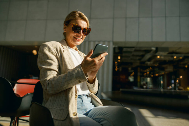 Lächelnde Geschäftsfrau mit Brille telefoniert in der Pause im modernen Büroflur - Foto, Bild