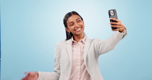 Teléfono, selfie y joven empresaria en un estudio con signo de paz para la personalidad tonta. Feliz, sonrisa y joven abogada india tomando una foto en el teléfono celular aislado por el fondo azul - Imágenes, Vídeo
