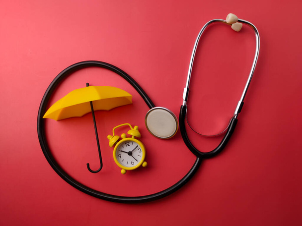 Górny widok stetoskop, budzik i żółty parasol na czerwonym tle - Zdjęcie, obraz