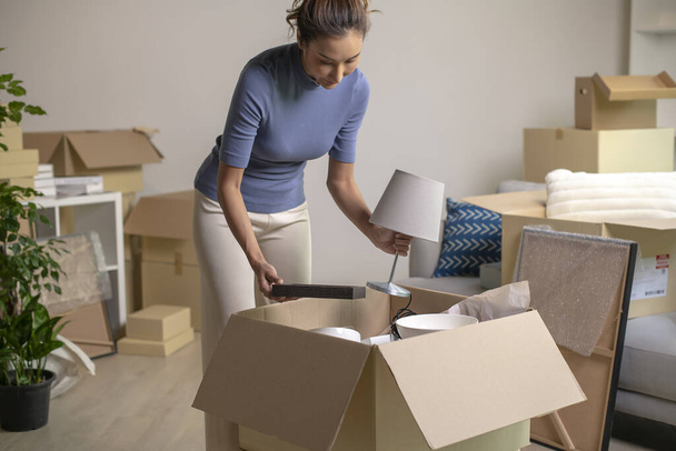 Joven mujer asiática mudándose a casa nueva desempacando sus pertenencias con cajas de cartón. - Foto, imagen