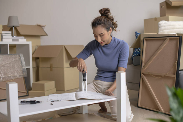 Een jonge Aziatische vrouw is het assembleren van meubels na het verhuizen naar een nieuw huis. - Foto, afbeelding