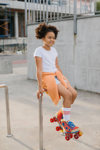 Afro-americká mladá dívka na kolečkových bruslích baví venku. Dívka se usměje a dívá se do kamery. - Fotografie, Obrázek