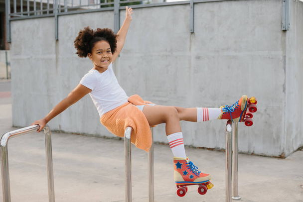 Afro-Amerikaans jong meisje in rolschaatsen hebben plezier buiten. Het meisje lacht terwijl ze naar de camera kijkt.. - Foto, afbeelding