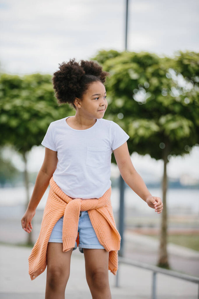Афроамериканская девушка катается на роликах на открытом воздухе, ребенок играет на роликовых коньках. - Фото, изображение