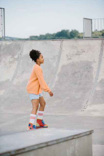 Cute African American little girl riding on roller skate in summer park. Kid enjoying outdoor sport in the park, Funny little girl playing on roller skate on road. sport learning outdoor concept - Φωτογραφία, εικόνα