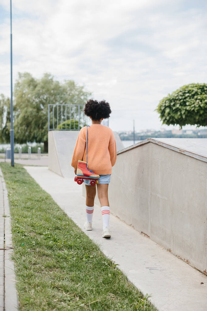 Mladá dívka přišla bruslit do skateparku. Africká americká dívka drží vinobraní válečky svázané tkaničkami. - Fotografie, Obrázek