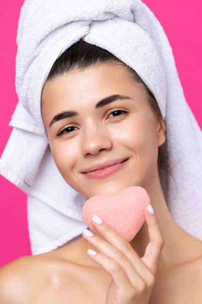 Красивая веселая привлекательная девушка с полотенцем на голове, держит губку в виде розового сердца. - Фото, изображение