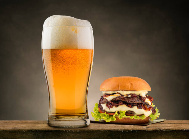Pint of lager beer with classic hamburger on wooden table. - Photo, Image