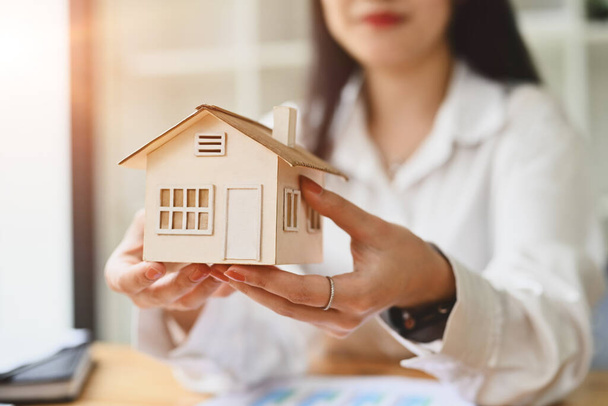 Женщина крупным планом держит модель дома с фонариком из окна. Концепция недвижимости, кредита, ипотеки и страхования. - Фото, изображение
