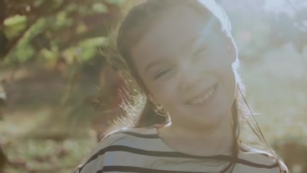 Menina bonita em um vestido de verão sorrindo cobrindo seu rosto com uma folha no parque. Verão, férias, conceito de infância feliz. Retrato de close-up - Filmagem, Vídeo