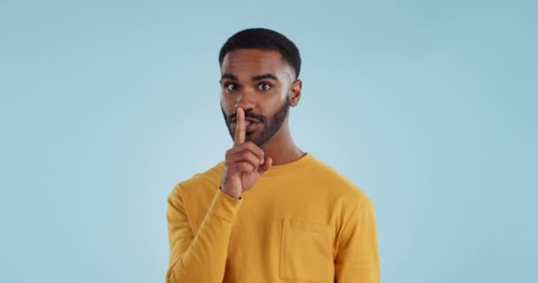 Secret, face and man with finger on lips in studio for quiet, privacy or hush news on blue background. Whisper, drama and portrait of guy model with confidential hand emoji for gossip or announcement. - Footage, Video