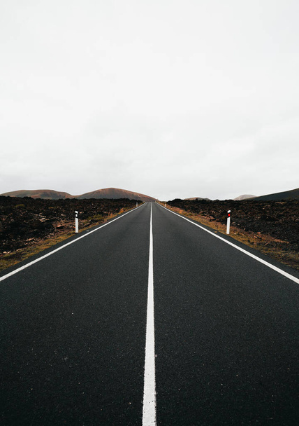 Вертикальное изображение пустой дороги с идеальными симметричными линиями в пасмурный день. Поездка на остров Лава - Лансароте (Канарские острова)).  - Фото, изображение