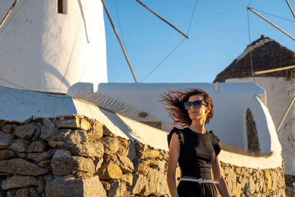 Junge Frau im schwarzen Kleid an den Windmühlen von Mykonos - Foto, Bild