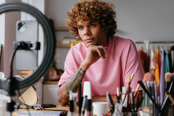 Confident young gay man looking at smart phone camera while recording make-up tutorial from home - Valokuva, kuva