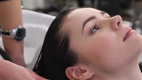 Close-up of shampooing in the beauty salon. Hair care in modern spa salon. Beauty salon, hair care and people concept - hairdresser hands washing happy young woman head. Shampoo for hair, beauty salon - Footage, Video