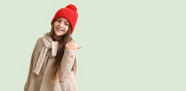 Cute little girl in winter clothes pointing at something on light background with space for text - Photo, Image