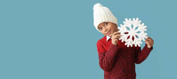 Lindo niño afroamericano en ropa de invierno cálido y con copo de nieve sobre fondo azul con espacio para el texto - Foto, Imagen