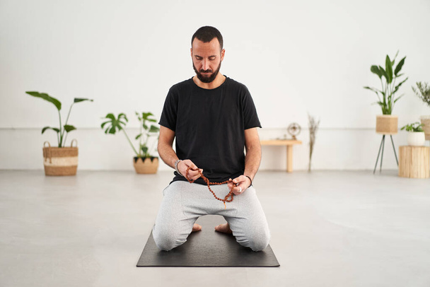 Caucasian yogi man beard doing meditation. Middle-aged male concentrating with eyes closed holds sandalwood yoga bead rosary. Concept of masculine wellness, body care and mental health. - Photo, Image
