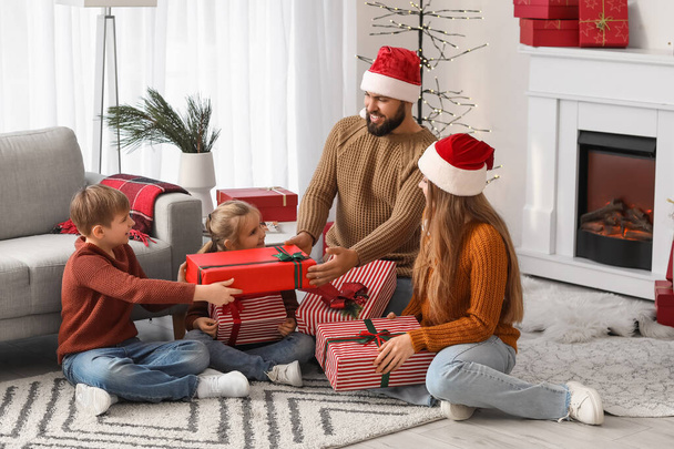 Happy parents in Santa hats and their little children with Christmas presents at home - Photo, Image