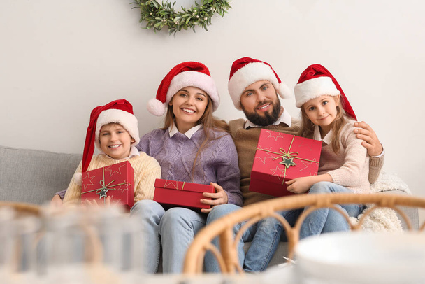 Szczęśliwa rodzina w Santa kapelusze z prezentów świątecznych siedzi na kanapie w domu - Zdjęcie, obraz