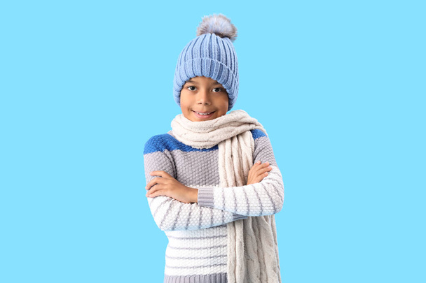 Χαριτωμένο Αφροαμερικανό αγόρι με ζεστά χειμωνιάτικα ρούχα σε μπλε φόντο - Φωτογραφία, εικόνα
