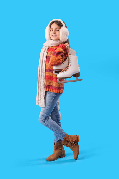 Cute little girl in winter clothes with ice skates on blue background - Φωτογραφία, εικόνα