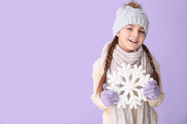 Cute little girl in winter clothes with big snowflake on lilac background - Фото, зображення