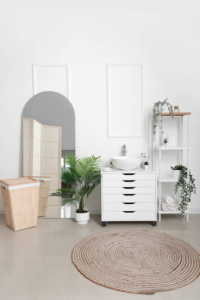 Interior of bathroom with chest of drawers, shelving unit, mirror and laundry basket - Photo, Image