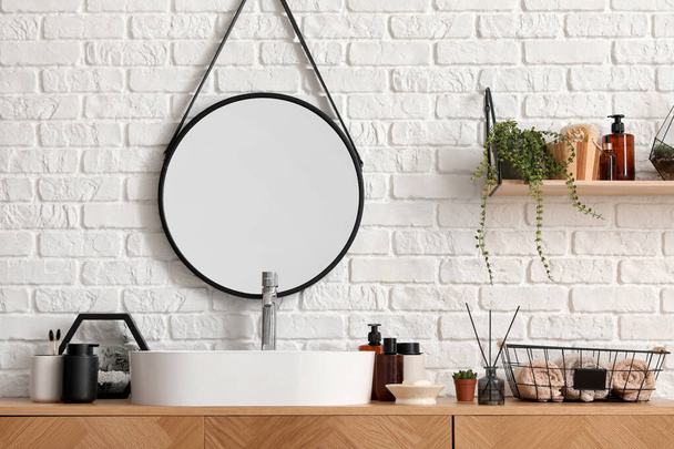 Vasca lavabo e accessori da bagno su armadio in legno vicino alla parete di mattoni bianchi - Foto, immagini