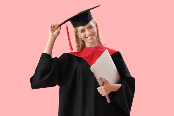 Estudiante graduada con portátil sobre fondo rosa - Foto, imagen
