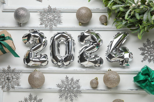 Σχήμα 2024 κατασκευασμένο από μπαλόνια φύλλο με μπάλες Χριστούγεννα, νιφάδες χιονιού και γκι υποκατάστημα σε λευκό φόντο - Φωτογραφία, εικόνα