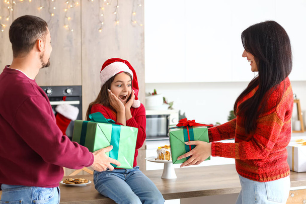 Surprised little girl receiving Christmas presents from her parents in kitchen - Photo, Image
