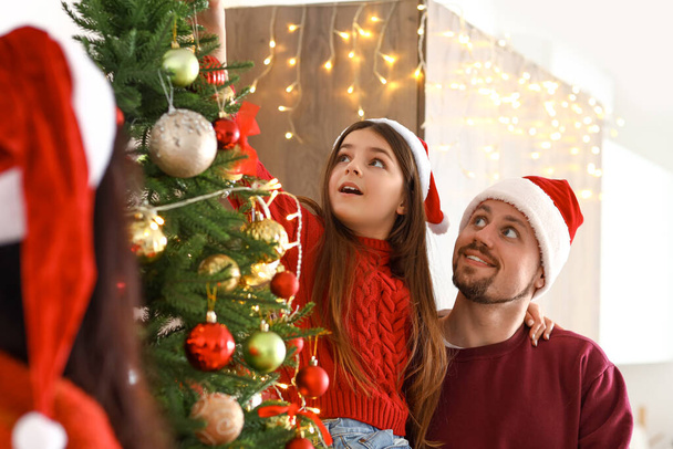 Niña con sus padres decorando el árbol de Navidad en casa - Foto, Imagen