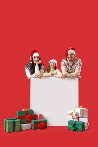 Boldog család karácsonyi ajándékok és üres poszter piros háttér - Fotó, kép