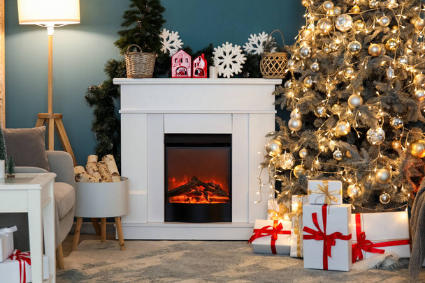 Interior of living room with Christmas tree, gift boxes, glowing lights, lamp, fireplace and armchair - Photo, Image