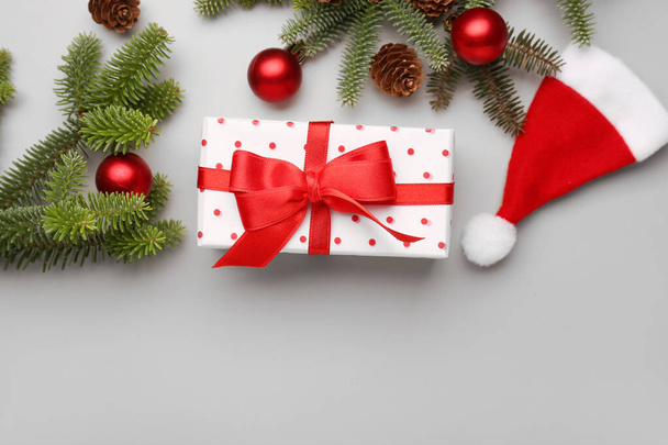 Christmas tree branches with gift box, balls and Santa hat on grey background - Zdjęcie, obraz