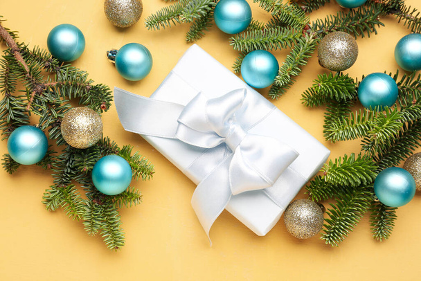Christmas tree branches with balls and gift box on yellow background - Photo, Image