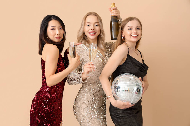 Jeunes femmes avec champagne et bal disco célébrant Noël sur fond beige - Photo, image