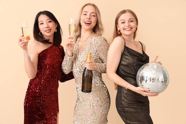 Young women with champagne and disco ball celebrating Christmas on beige background - Photo, Image