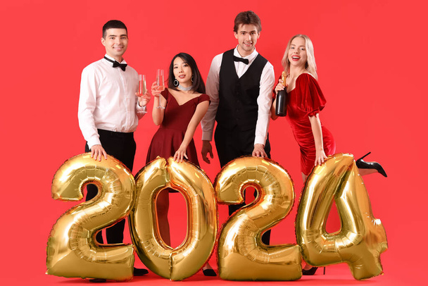 Giovani con champagne e palloncini a forma di figura 2024 su sfondo rosso - Foto, immagini