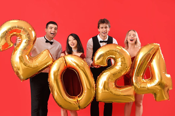 Νέοι με μπαλόνια σε σχήμα εικόνας 2024 σε κόκκινο φόντο - Φωτογραφία, εικόνα