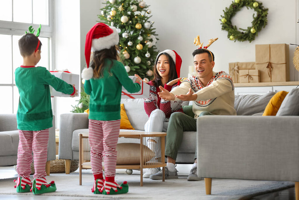 Gelukkige ouders ontvangen kerstcadeaus van hun kleine kinderen thuis - Foto, afbeelding