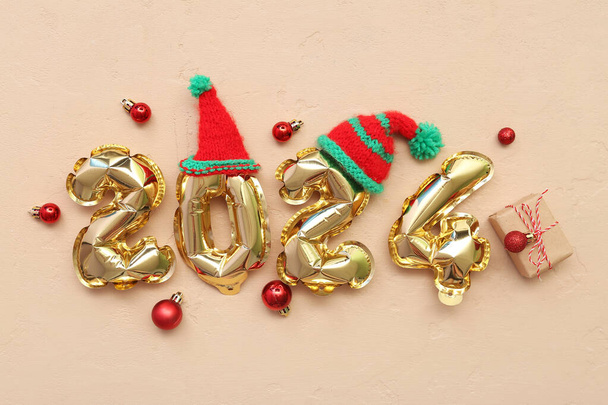 Folyo balonlardan, Noel balonlarından, hediye kutusundan ve bej arka plandaki şapkalardan oluşan 2024 figürlü kompozisyon - Fotoğraf, Görsel