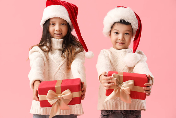 Niedliche kleine Kinder mit Weihnachtsgeschenken auf rosa Hintergrund - Foto, Bild
