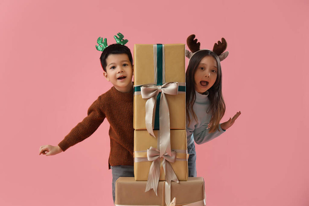 Lindos niños pequeños con regalos de Navidad sobre fondo rosa - Foto, Imagen