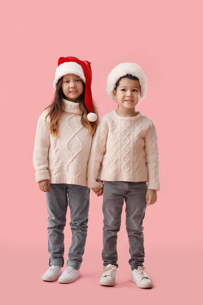 Cute little children in winter sweaters and Santa Claus hats on pink background - Photo, Image