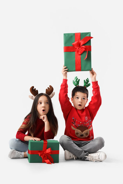 Удивленные маленькие дети с рождественскими подарками сидя на белом фоне - Фото, изображение