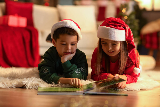 サンタのかわいい子供たちはクリスマスイブで自宅で物語を読みます - 写真・画像