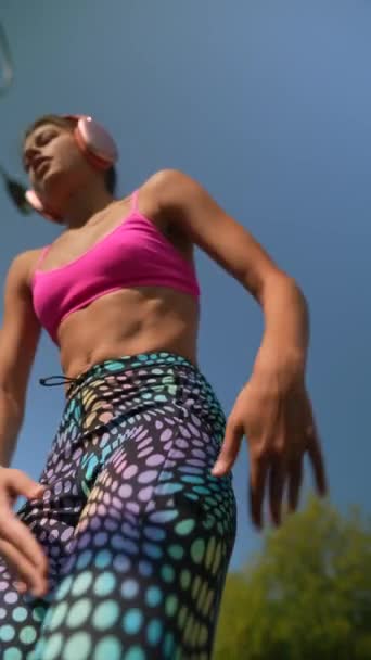 Een energieke jonge vrouw, met een koptelefoon op, doet stretching oefeningen in de buitenlucht in de stad. Hoge kwaliteit 4k beeldmateriaal - Video