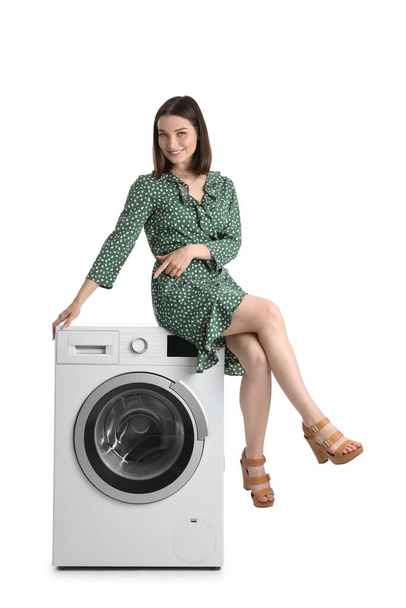 Jovem mulher sentada na máquina de lavar roupa contra fundo branco - Foto, Imagem